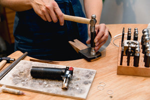Student uses tools at the workshop bench to shape their handcrafter piece of jewellery made in workshop