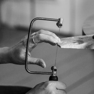 Student hand sawing silver plate to create unique piece in jewellery making workshop
