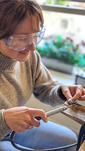 Woman uses electric sander to smooth handmade wedding ring in workshop